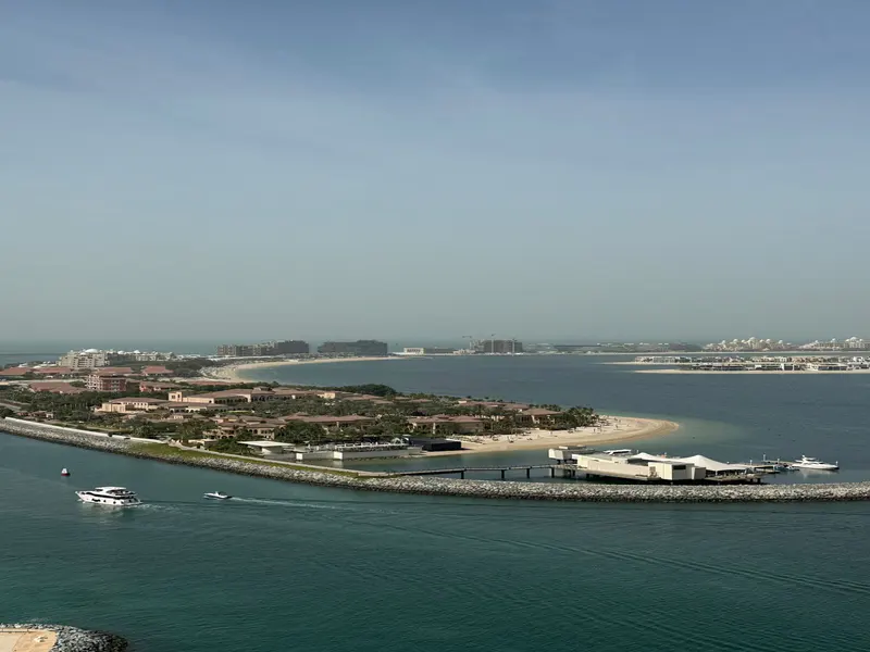 Aerial view of Palm Jumeirah, Dubai, with luxury villas, sandy beaches, and turquoise water. Yachts sail along the breakwater.