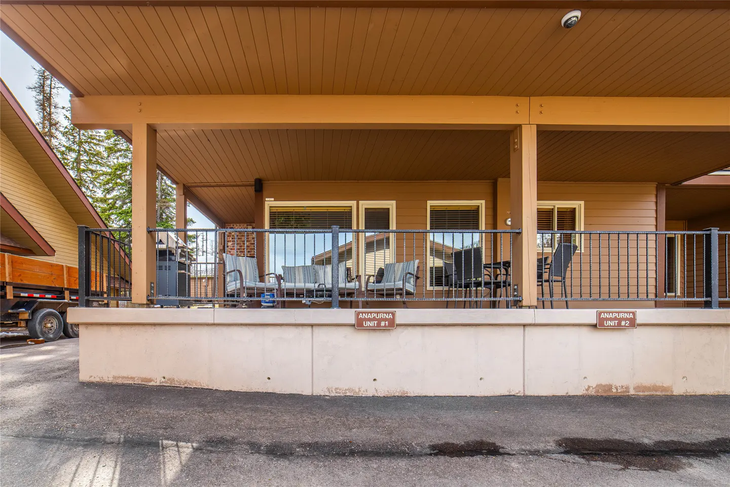 Exterior view of a brown condo with a patio, black metal railing, and outdoor furniture. "Anapurna Unit #1" and "Anapurna Unit #2" signs are visible.