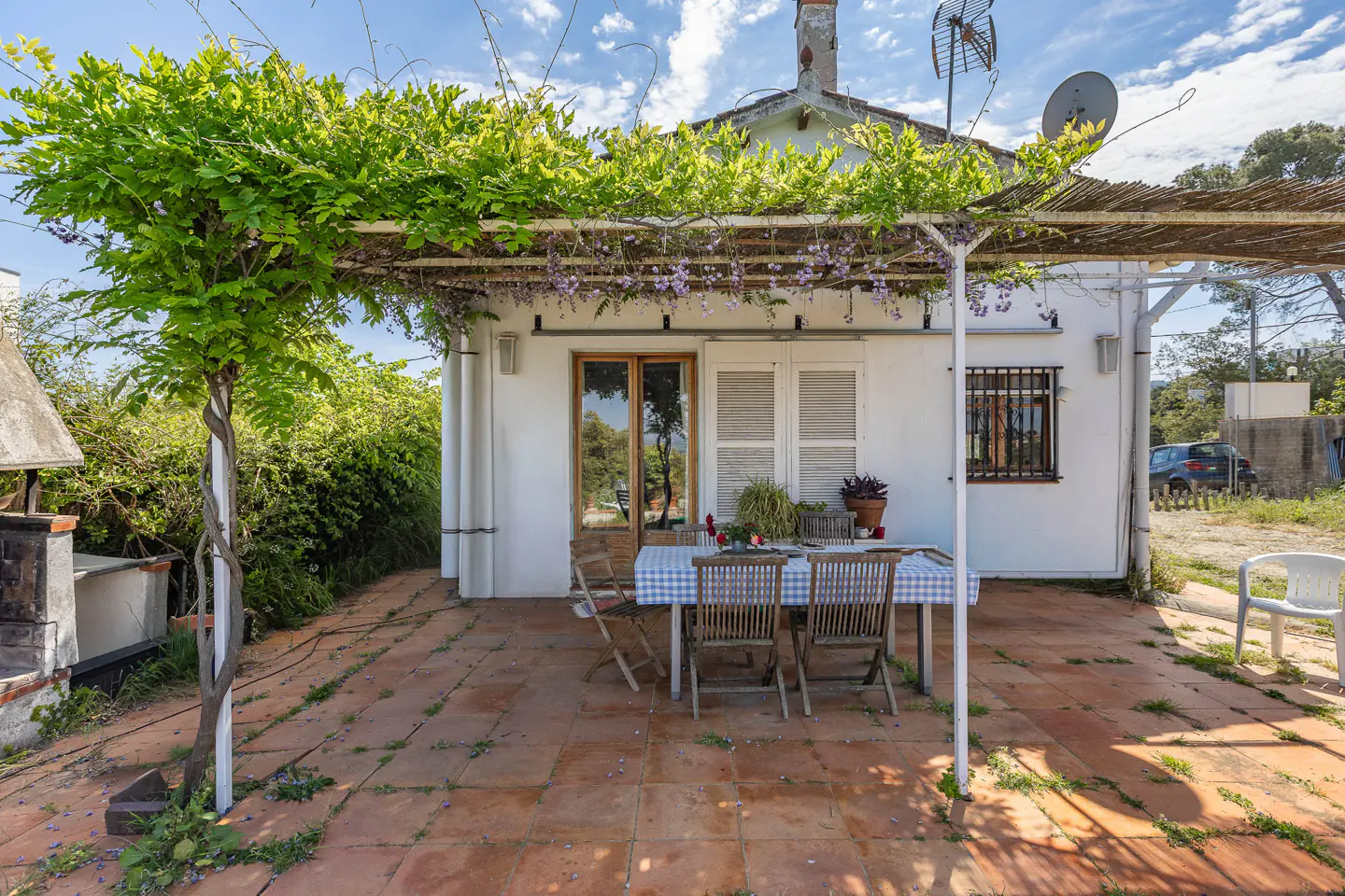 Outdoor patio with a table and chairs under a green vine-covered pergola, attached to a white house with a red tile roof.