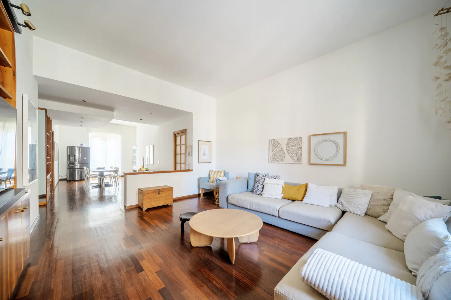 Bright living room with hardwood floors, a large sectional sofa, and a round coffee table. Art hangs on the white walls.
