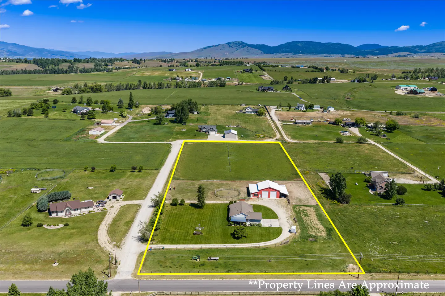 Aerial view of a rural property outlined in yellow, featuring a house, red barn, and large green fields under blue skies.