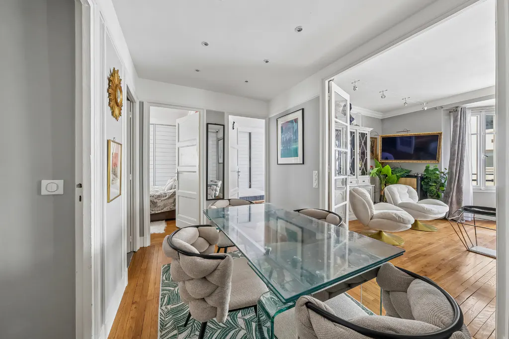 A bright, airy apartment interior with a glass dining table, upholstered chairs, and an open living room with white swivel chairs.