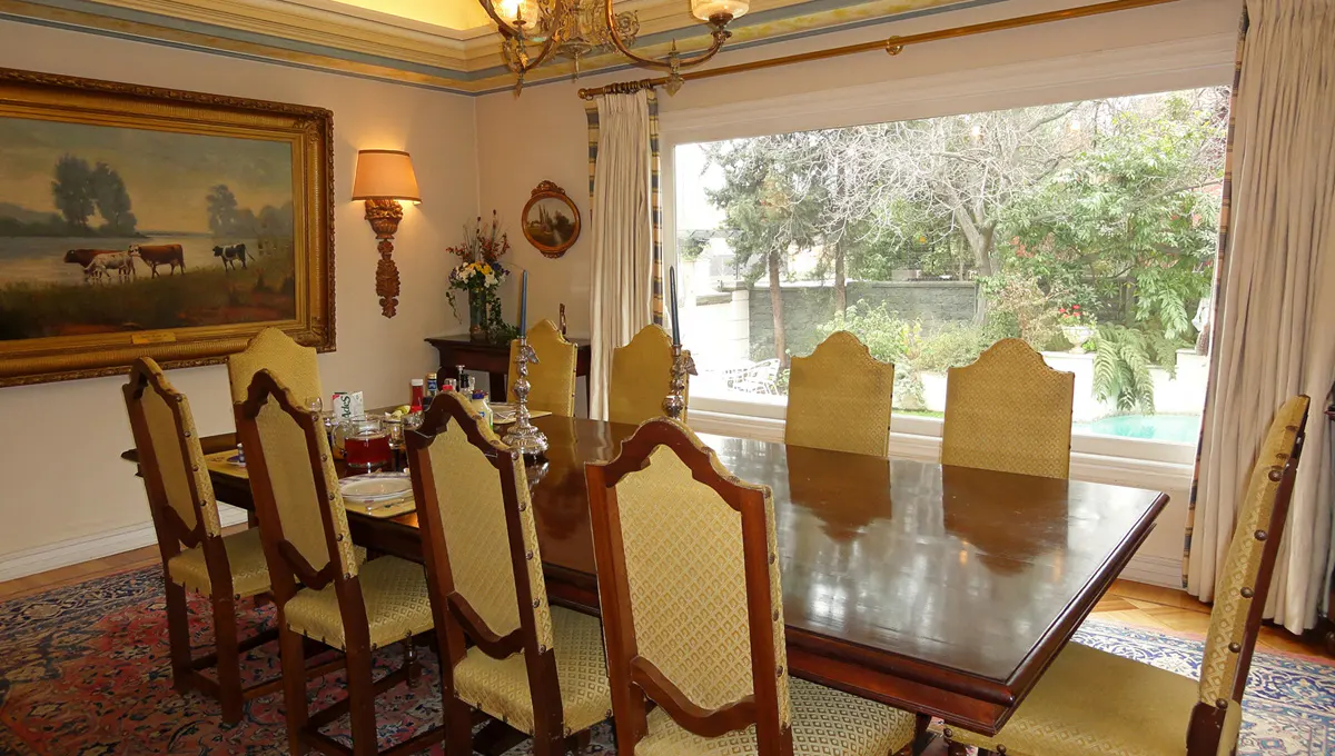 Formal dining room with a dark wood table, yellow upholstered chairs, and a large window overlooking a green backyard with a pool.