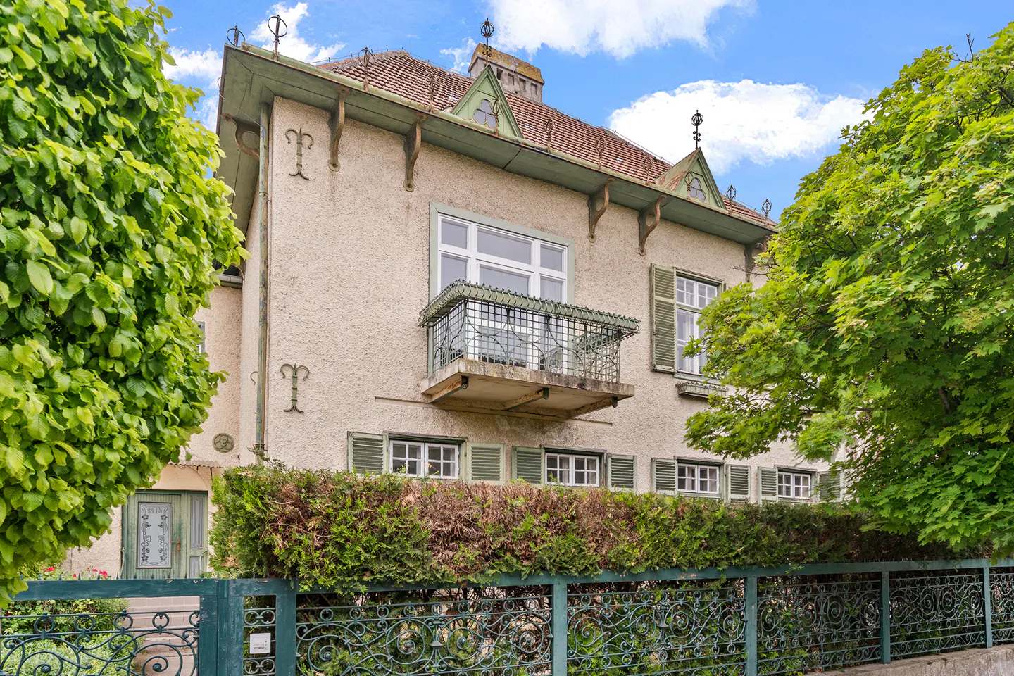 A beige two-story house with green trim, a balcony, and a green wrought-iron fence.