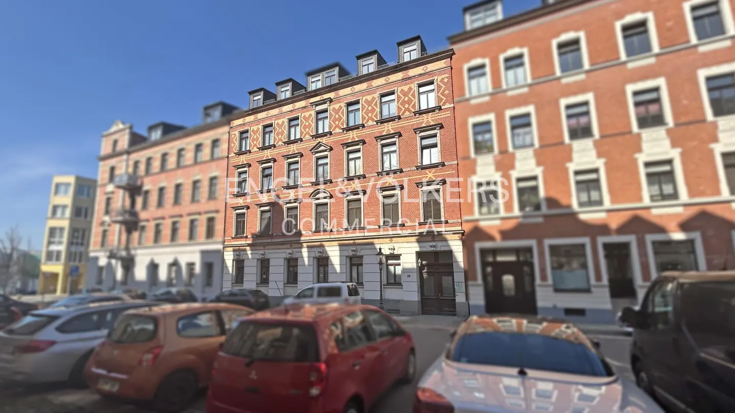 A four-story red brick building with white trim and dormer windows, cars parked in front.
