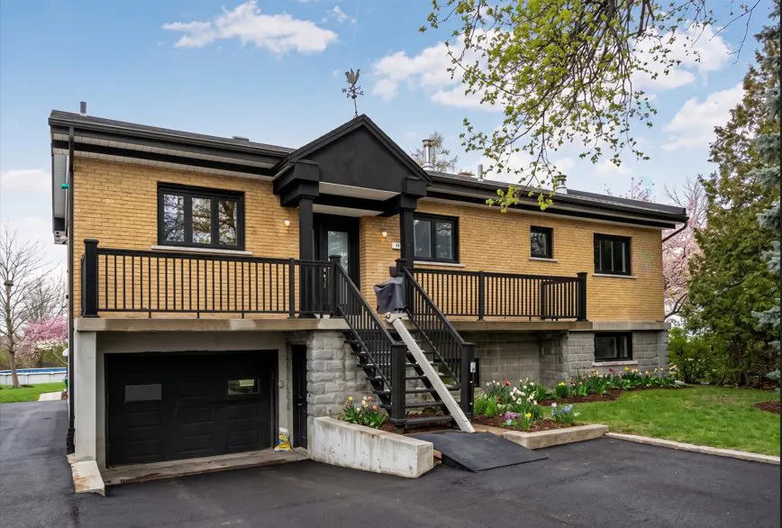 Two-story yellow brick house with black trim, a black garage door, and a ramp leading to the front door.