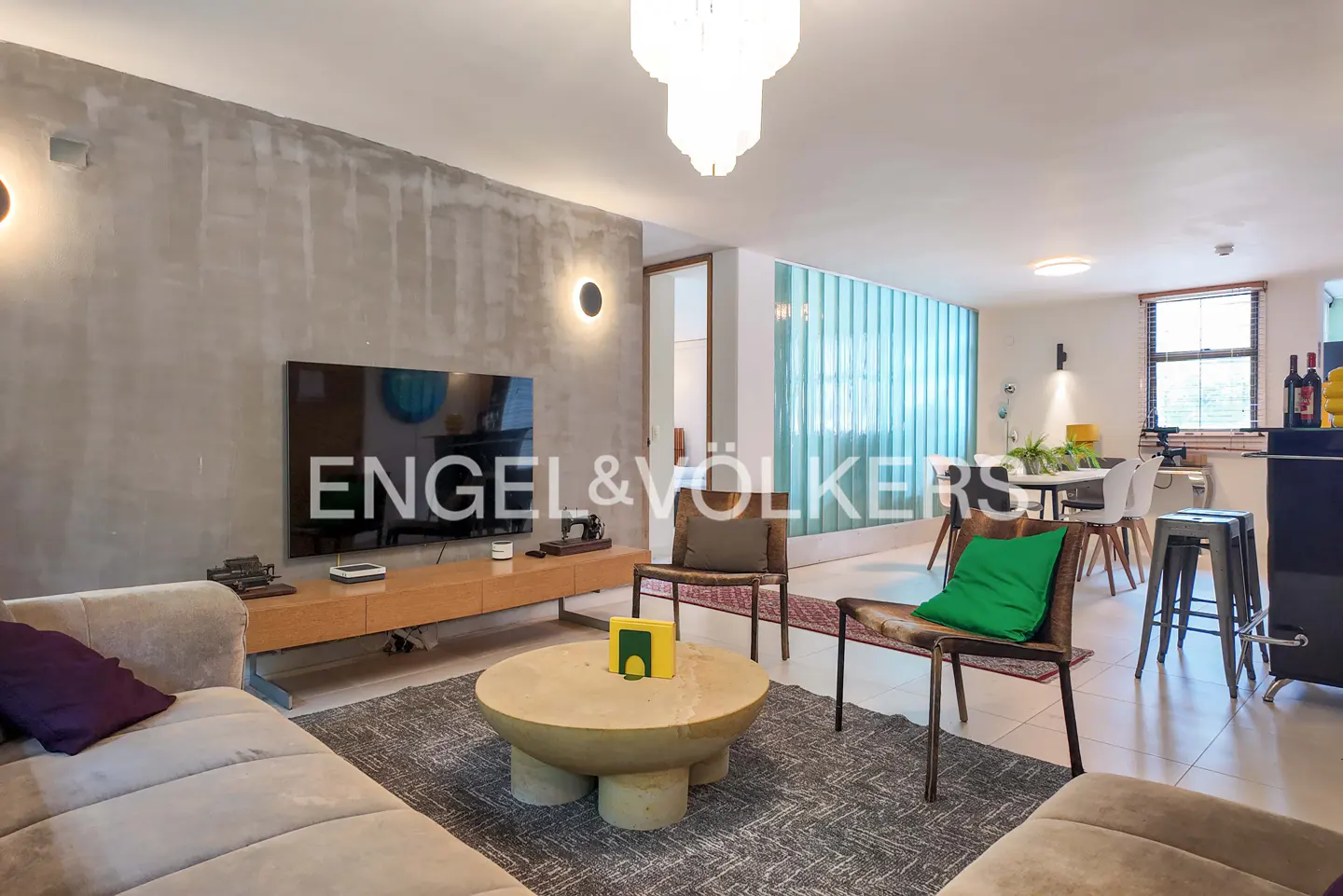 Bright, modern living room with a gray sofa, round coffee table, and a TV on a wooden console against a textured gray wall. Dining area visible in the background.
