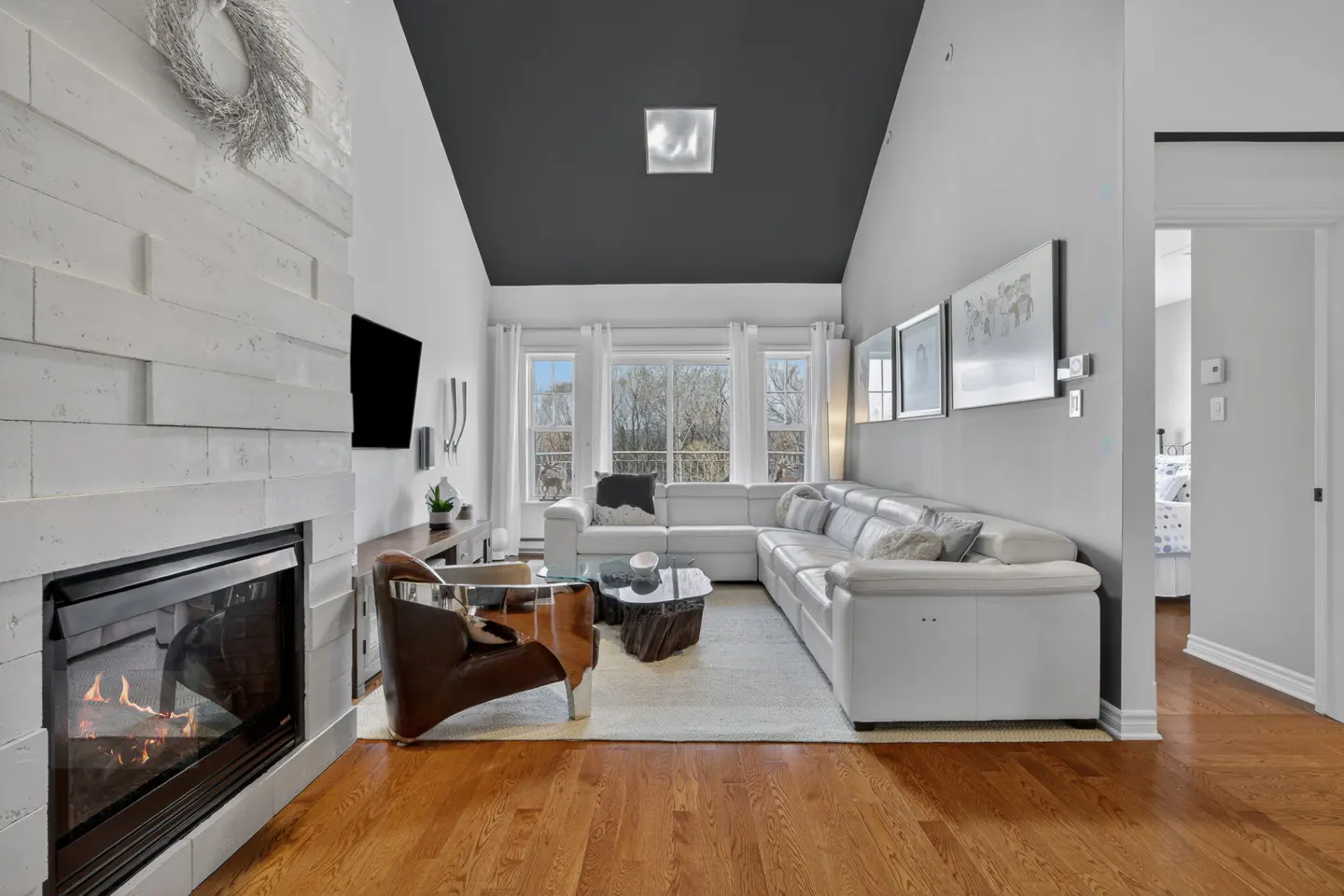 Bright living room with a white sectional sofa, fireplace, and hardwood floors. A dark gray ceiling adds contrast to the room.