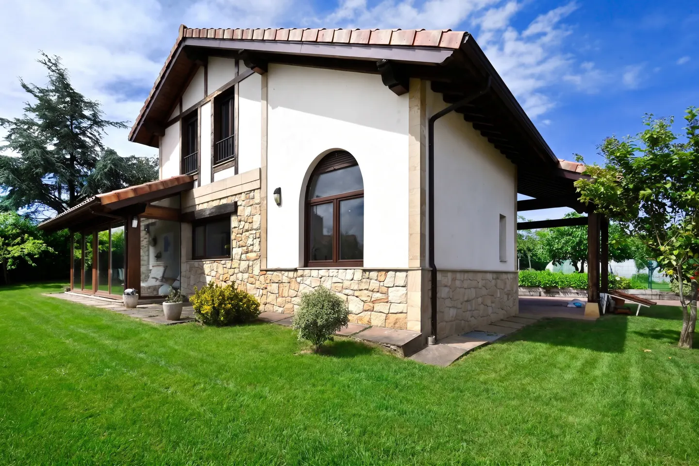 Two-story house with white stucco and stone facade, brown trim, and green lawn under a blue sky.