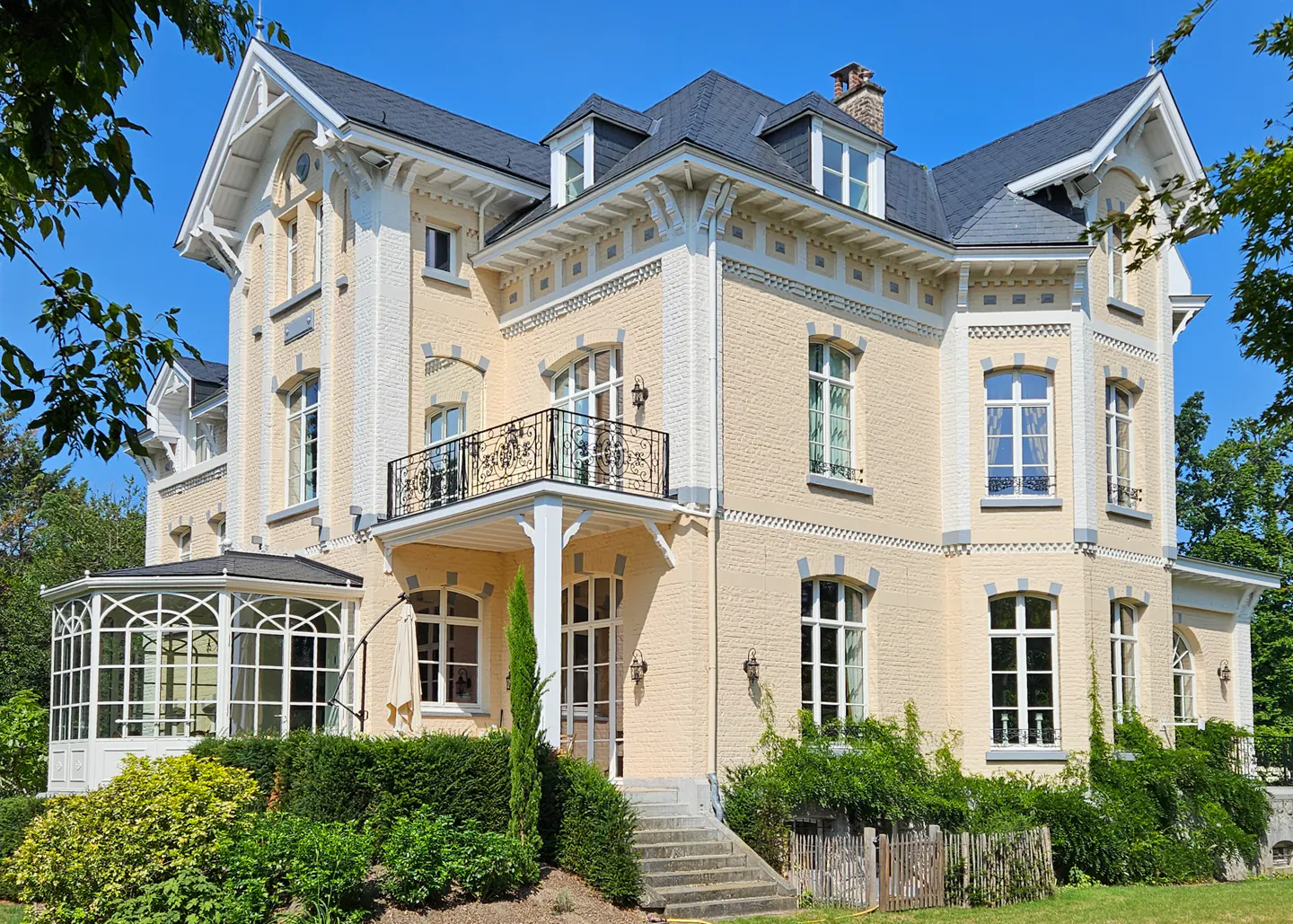 A three-story, light-yellow brick house with a black roof and white trim on a sunny day.
