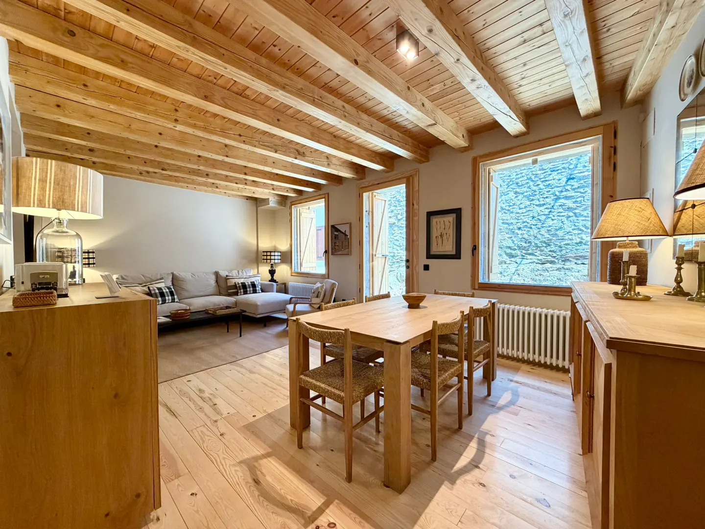 Living room with wood floors, exposed beam ceiling, dining table with six chairs, and a sofa in the background.