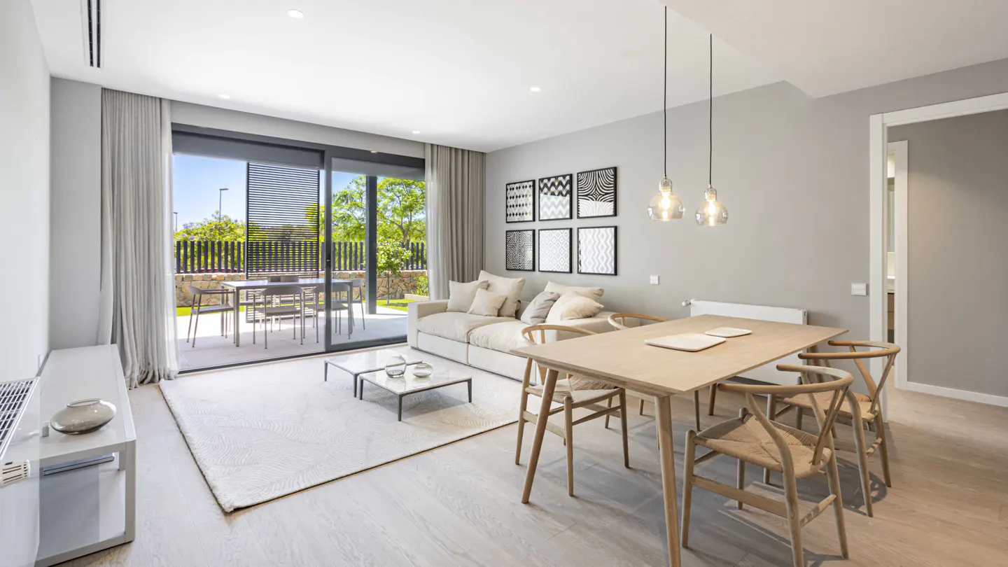 Bright, modern living room with a beige sofa, wood dining table, and sliding glass doors to a patio. Black and white art hangs on the gray wall.