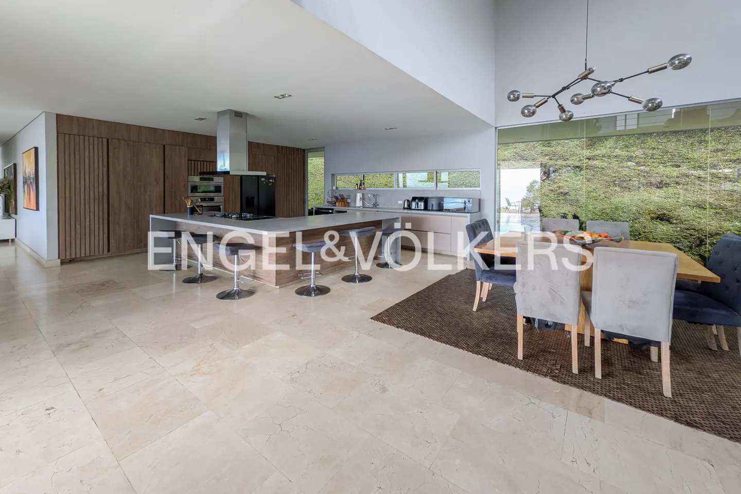 Open-concept kitchen and dining area with marble floors. Island with stools, wood cabinets, and a dining table with blue chairs.