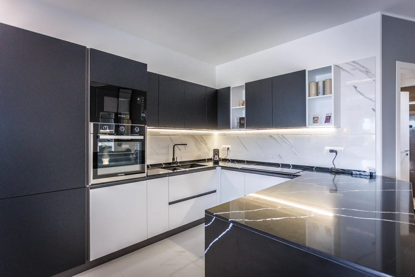 Modern kitchen with black and white cabinets, marble countertops, and a black island with white veining.