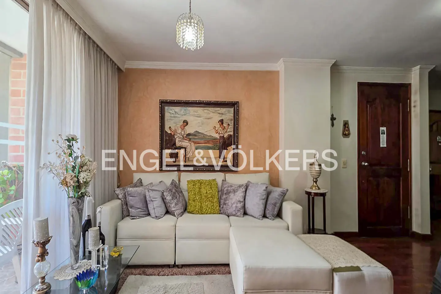 Living room with a white sectional sofa, decorative pillows, and a painting above. A chandelier hangs from the ceiling.