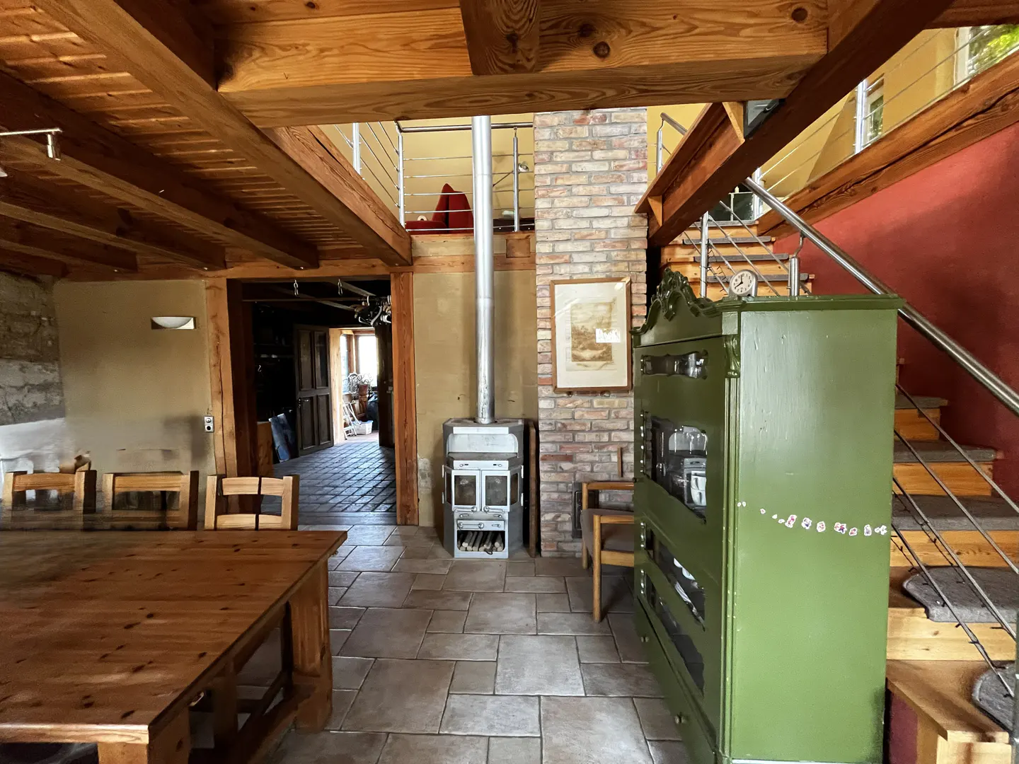 Interior view of a rustic home with exposed wood beams, a brick fireplace, and a green cabinet near a staircase.