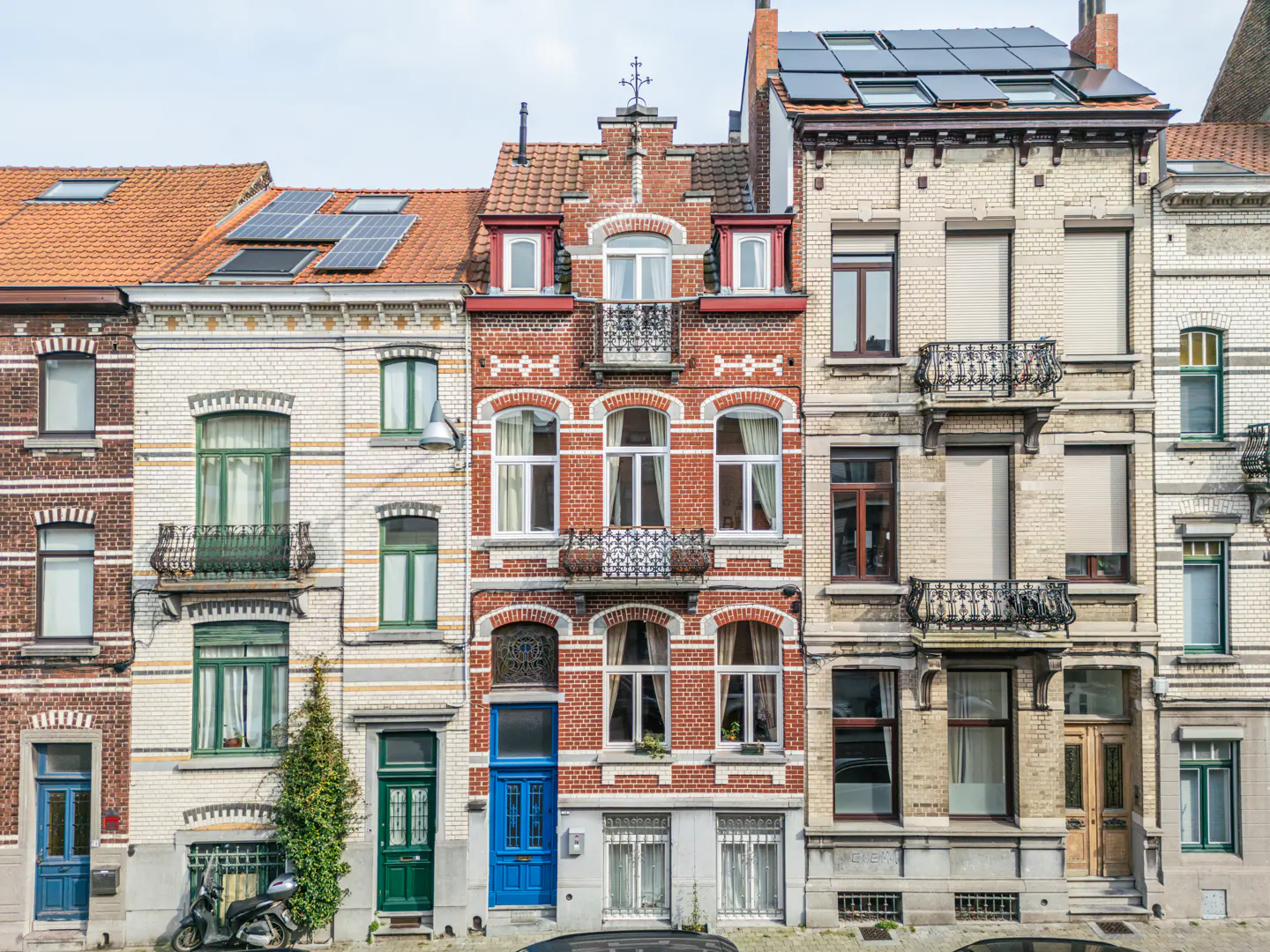Row of colorful brick townhouses with balconies and solar panels under a cloudy sky.
