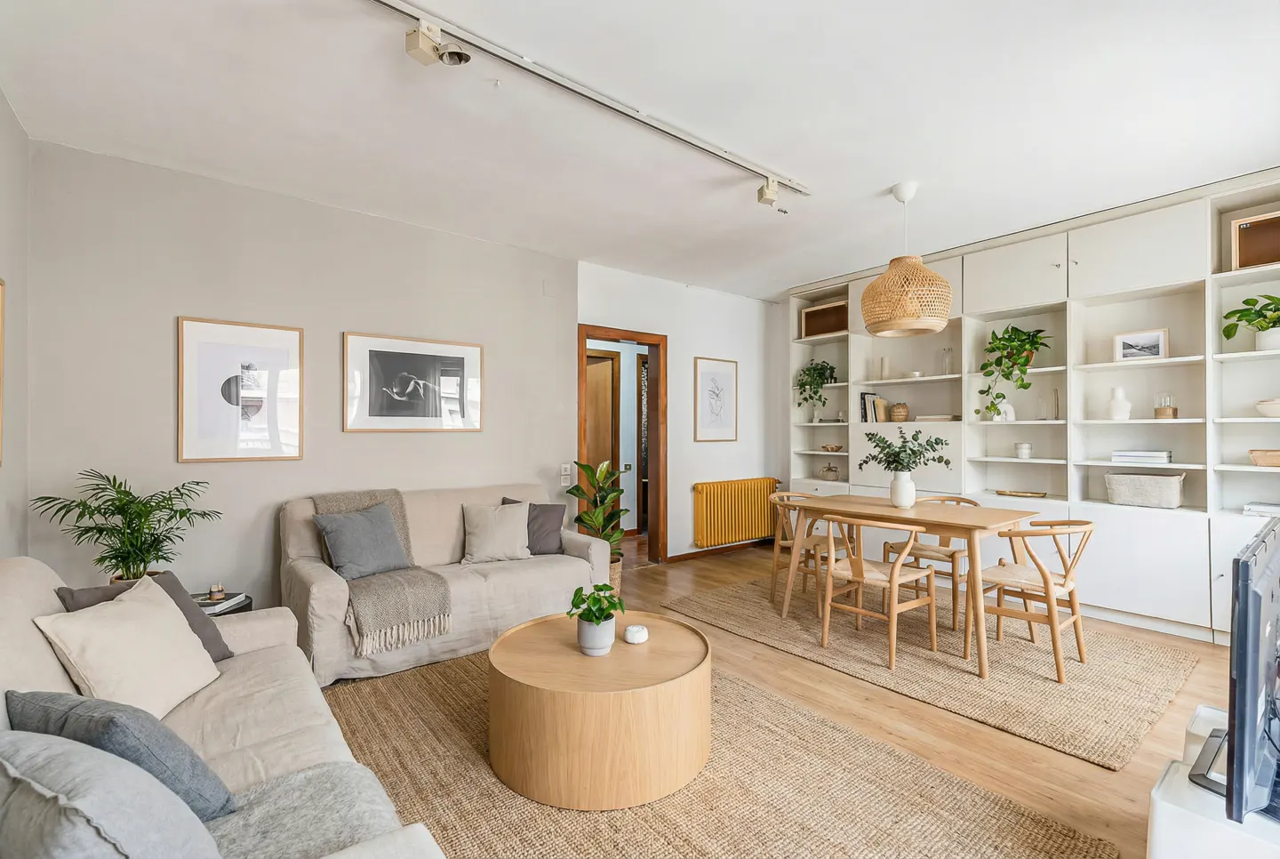 Living room with two sofas, a round coffee table, a dining table with chairs, and a white bookshelf.