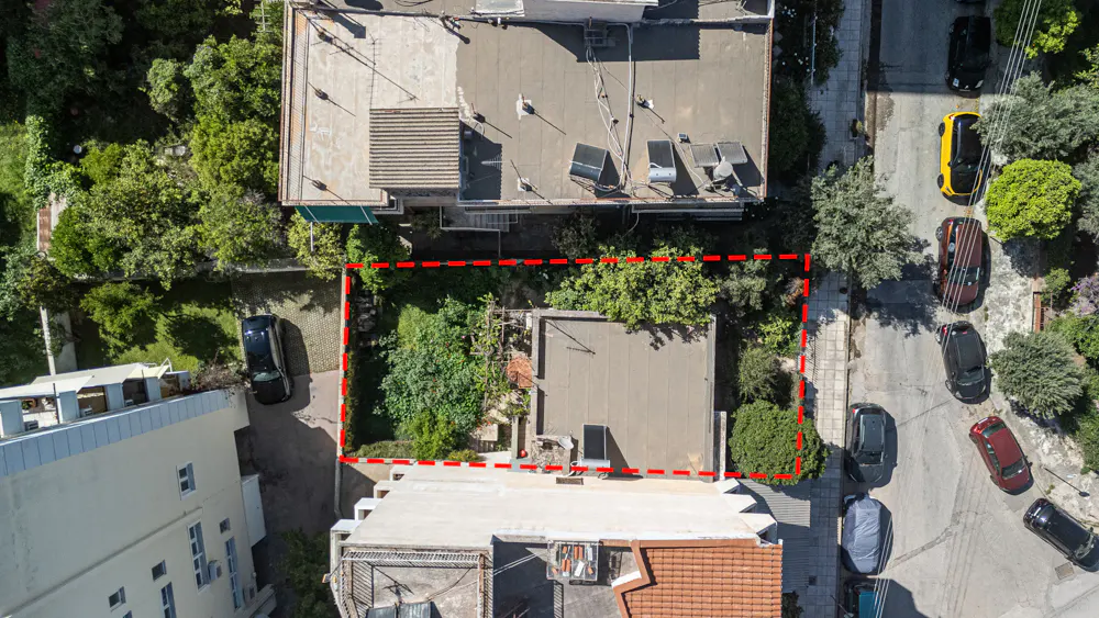 Aerial view of a property outlined in red, surrounded by buildings, trees, and parked cars on a street.