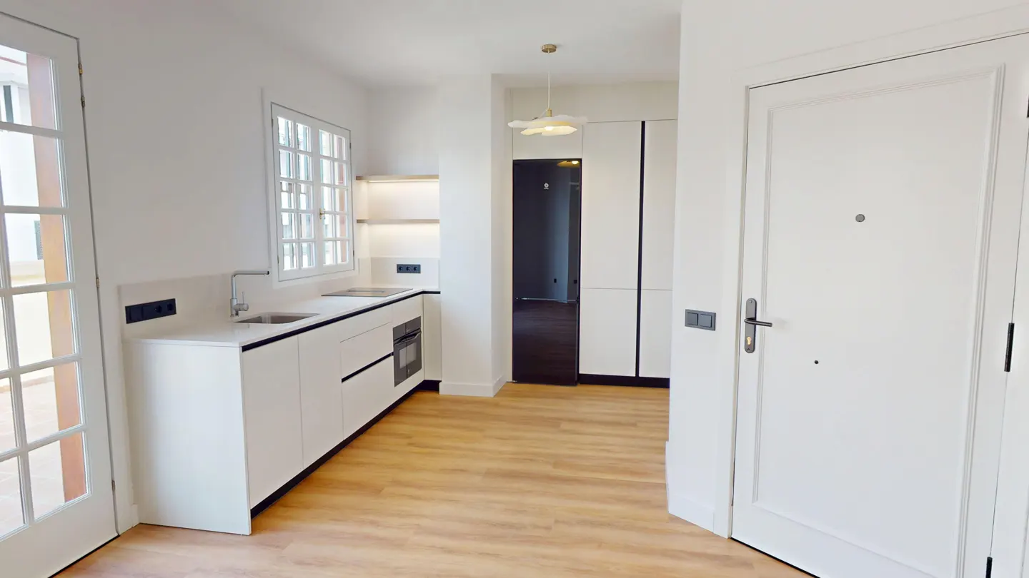Bright, modern kitchen with white cabinets, light wood floors, and a white door. A window sits above the sink, and a pendant light hangs from the ceiling.