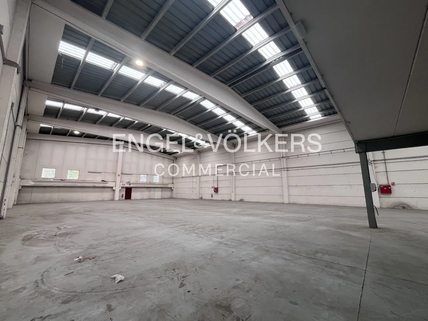 A large, empty warehouse with a concrete floor and a high, metal ceiling with skylights.