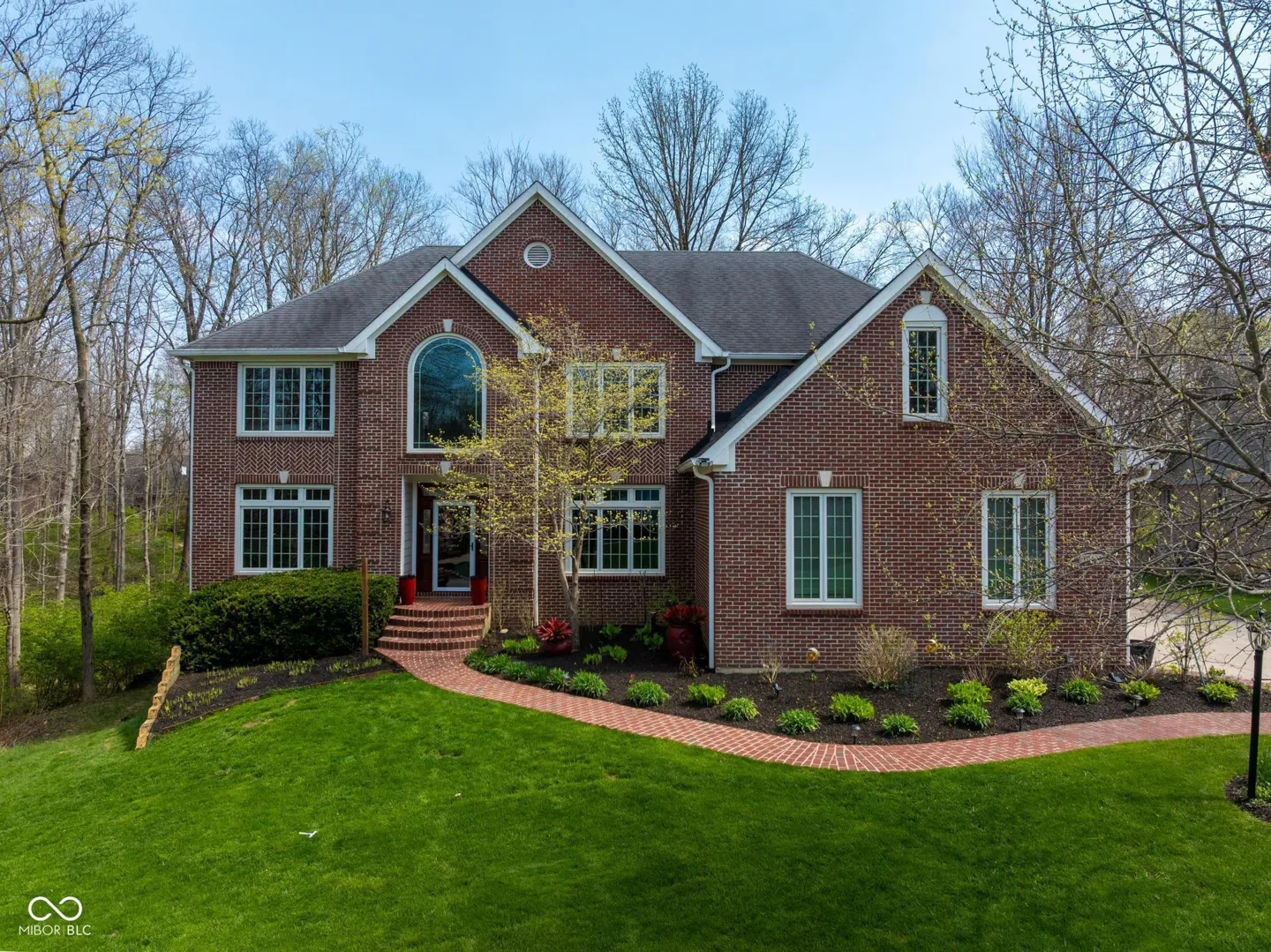 Two-story brick house with a green lawn and brick walkway on a sunny day.