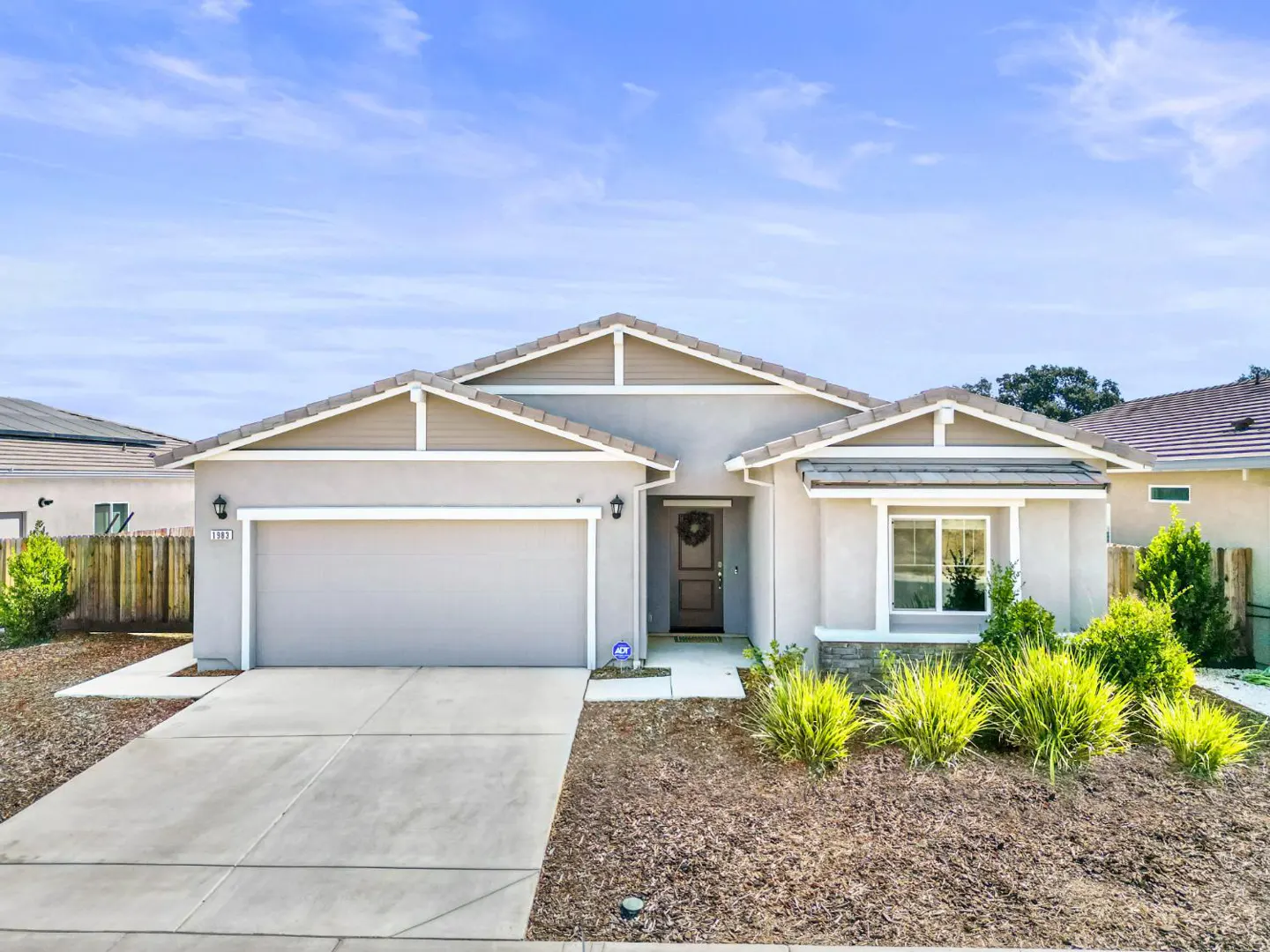 Beige single-story home with a gray roof, a two-car garage, and a concrete driveway under a blue sky.