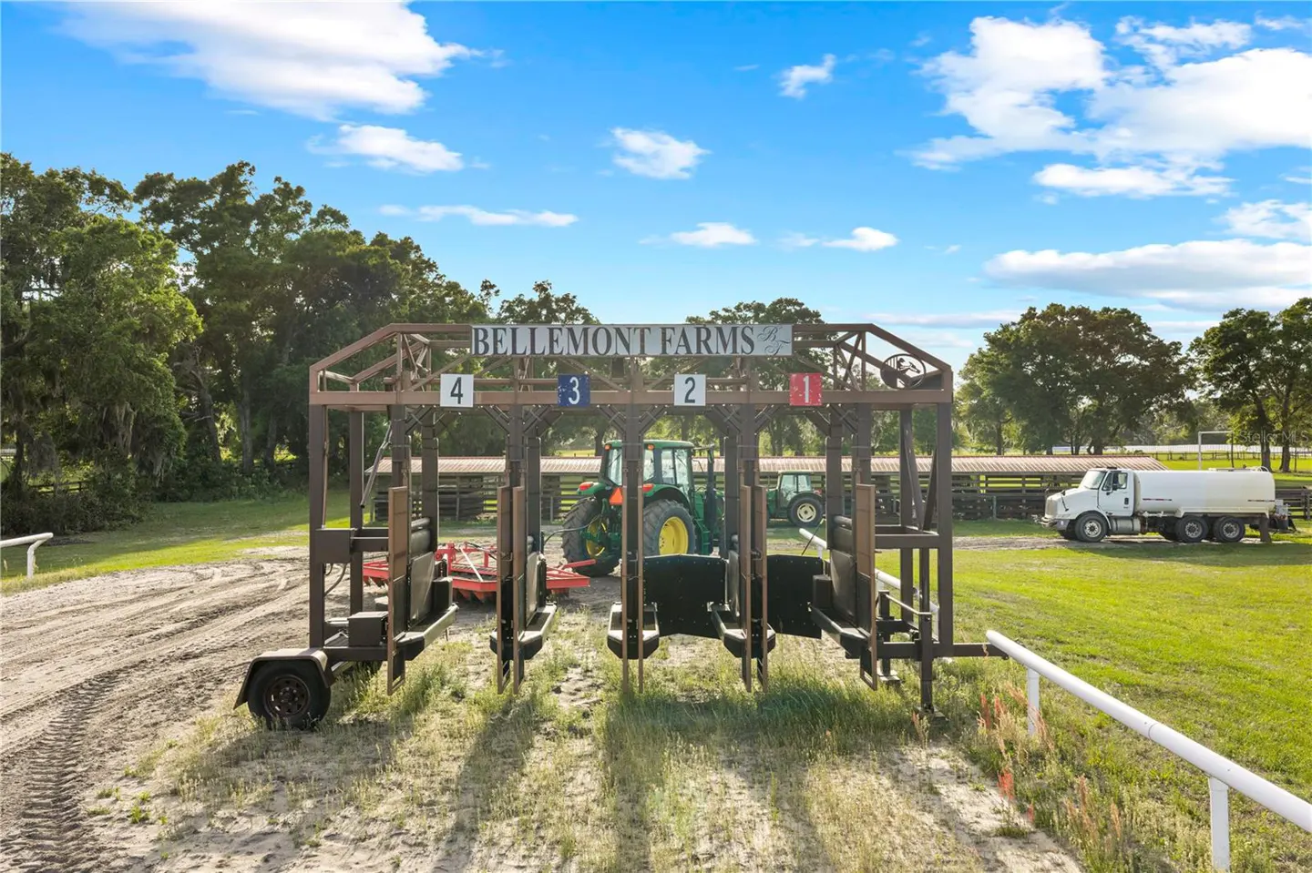 Bellemont Farms horse racing starting gate with tractors and a water truck in the background on a sunny day.