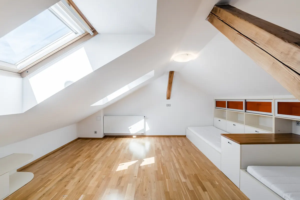 Bright attic room with wood floors, white walls, skylights, and built-in beds with orange accents.