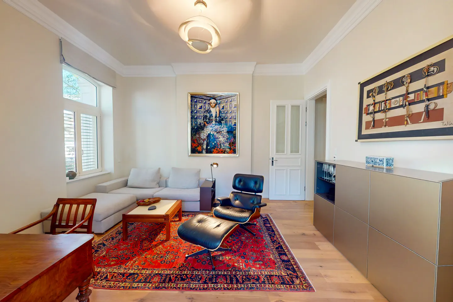 Living room with a gray sofa, black chair, and red rug. Art hangs on the white walls.