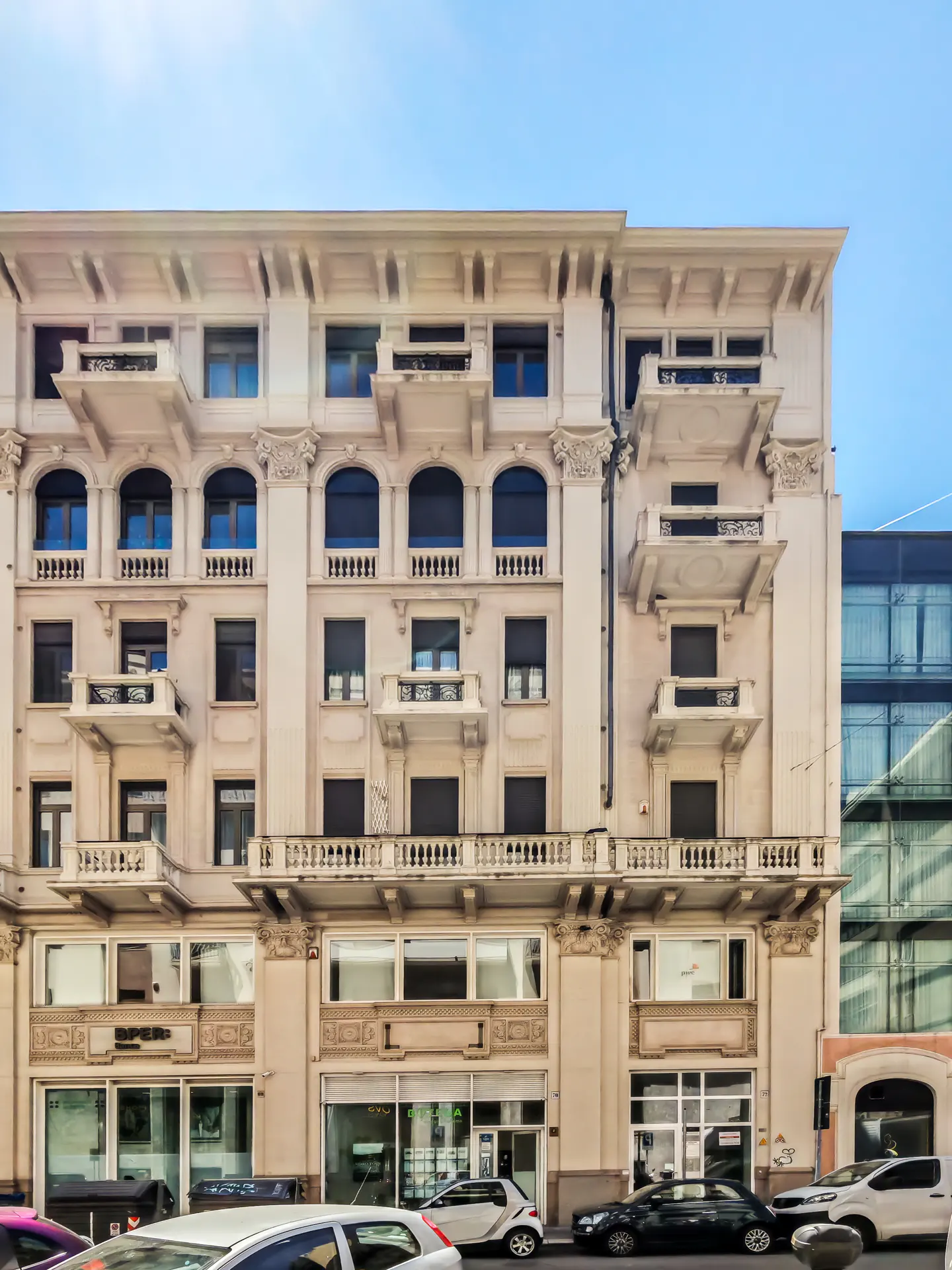 A classic beige multi-story building with ornate balconies and arched windows above ground-floor storefronts.