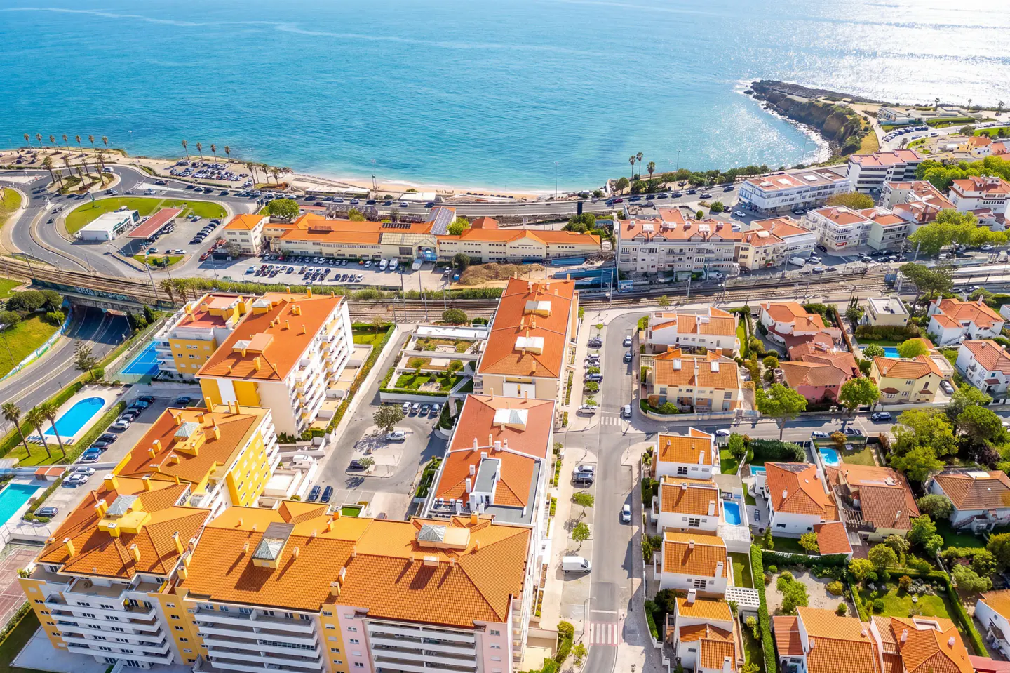 Aerial view of a coastal town with orange-roofed buildings near a blue ocean and sandy beach.