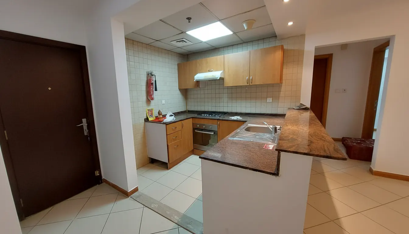 A kitchen with light wood cabinets, granite countertops, and tiled walls. A brown door is on the left.