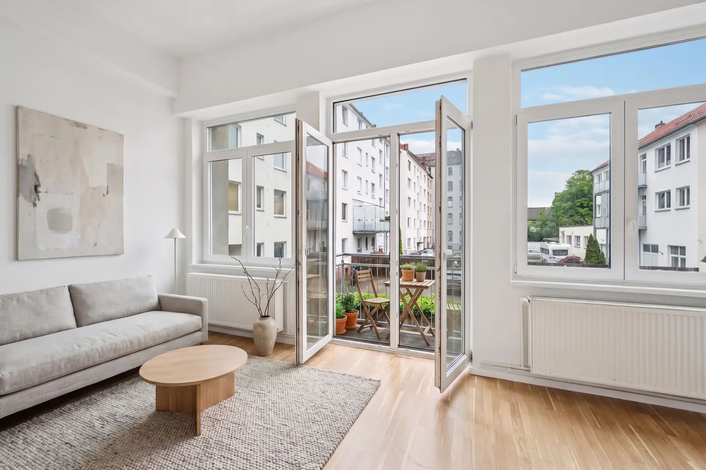 Bright living room with a gray sofa, wood table, and open doors to a balcony with a table and chairs.