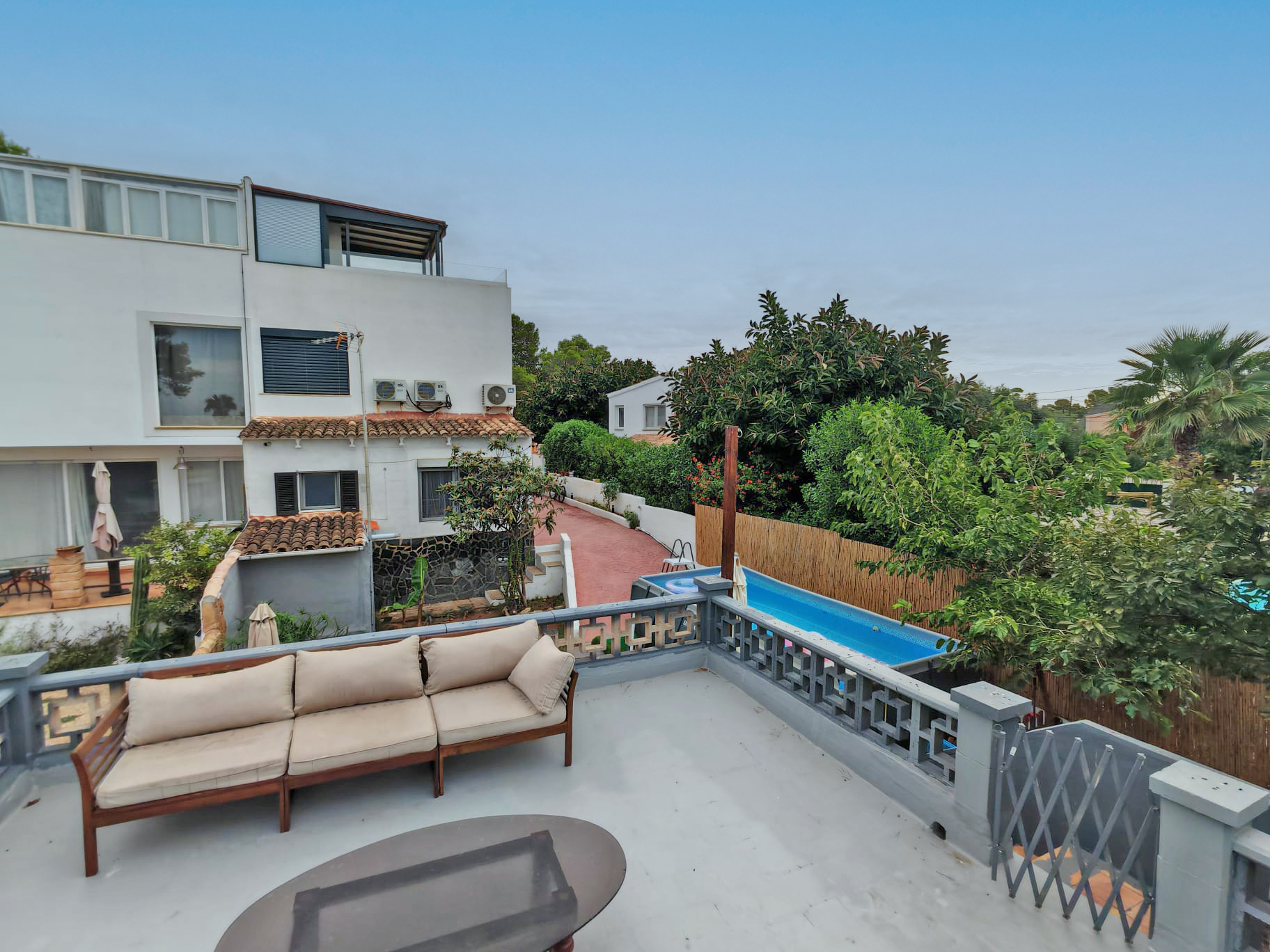Rooftop terrace with a beige sectional sofa and coffee table, overlooking a backyard with a swimming pool and greenery. [AI-generated text] [KI-modifiziert]
