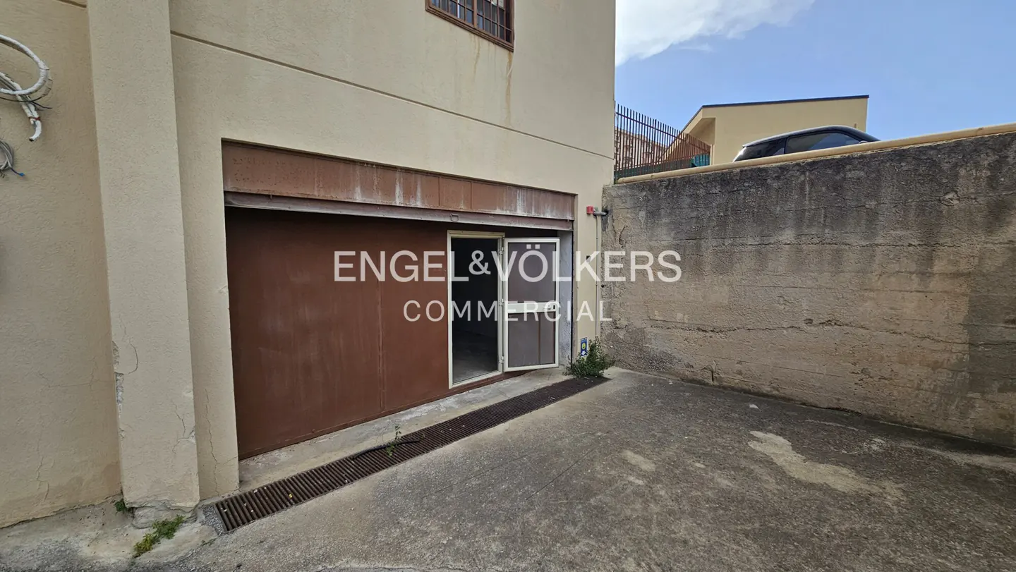 Exterior view of a brown garage door with Engel & Volkers logo, next to a concrete wall and a beige building.