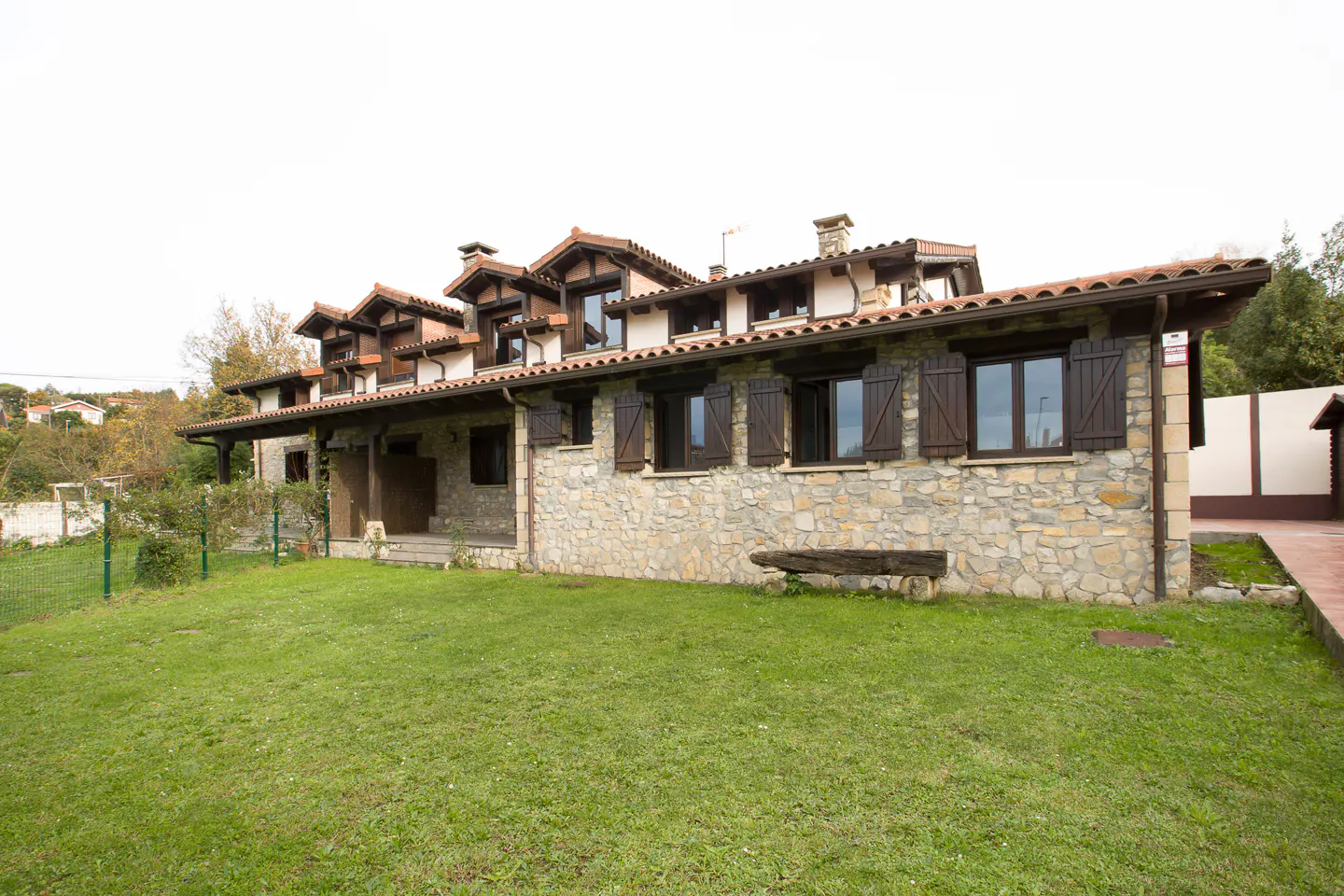 Stone house with brown shutters and a red tile roof, surrounded by a green lawn.