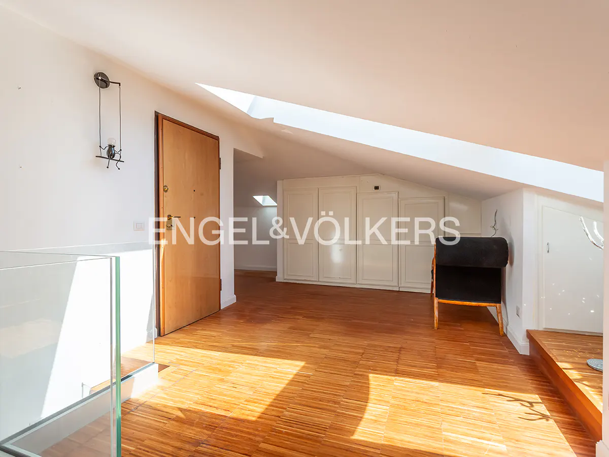 Attic room with wood floors, white walls, and a skylight. A wooden door is on the left, and a black chair is on the right.