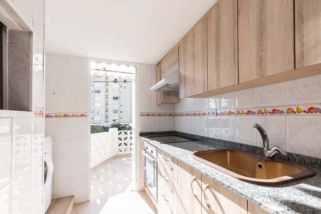 Bright kitchen with light wood cabinets, granite counters, and a bronze sink. A balcony with a view of a building is visible.