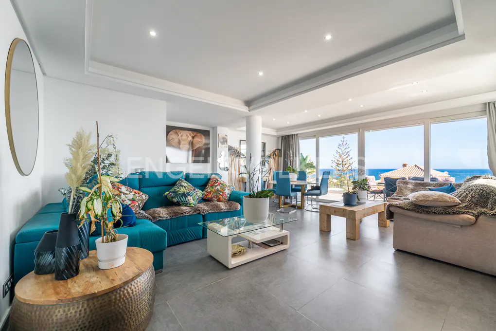 Bright living room with ocean view features a teal sofa, dining table, and large windows.