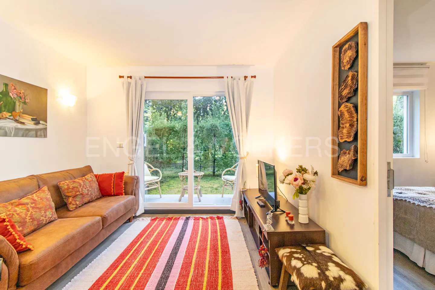 Living room with brown sofa, striped rug, TV, and sliding glass doors to a green yard. Artwork on the wall.