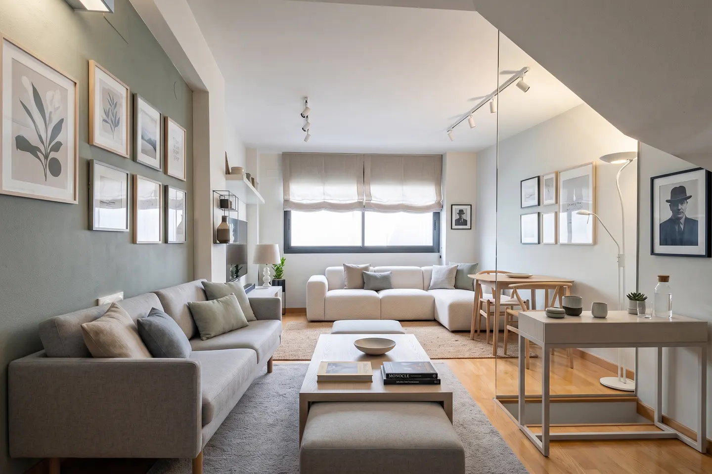 Modern living room with a sage green accent wall, grey sofa, white sectional, wooden dining set, and framed wall art.