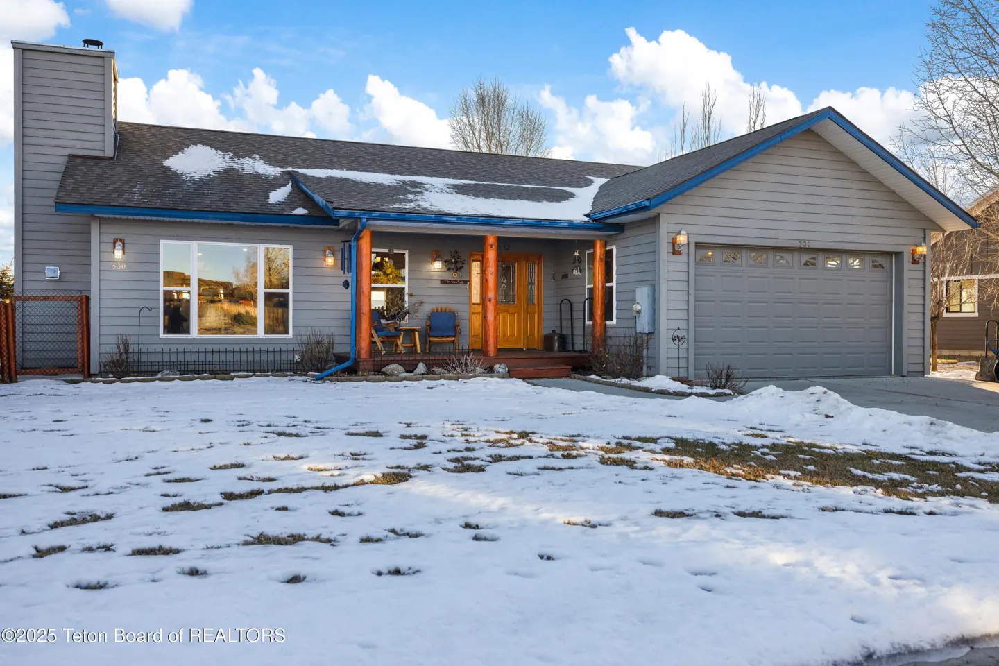 Gray house with a brown door and porch columns, a gray garage door, and snow on the lawn.