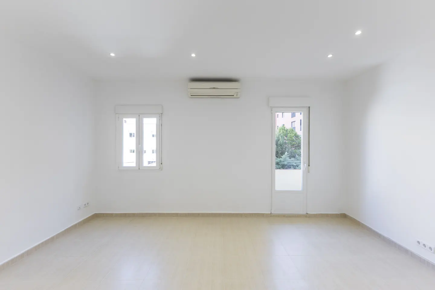 Bright, empty room with white walls, beige tile floor, window, door to outside, and air conditioner.