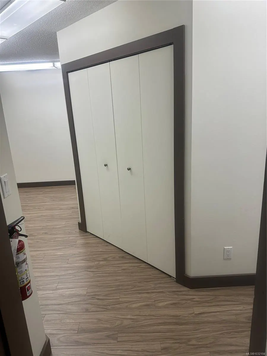 Interior shot of a room with wood-look flooring, white walls, and a closet with four white doors and dark trim. A fire extinguisher is visible.