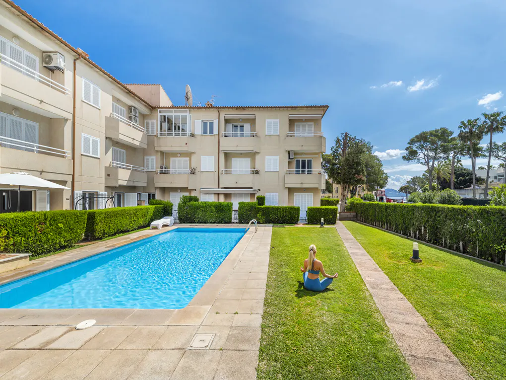 Apartment complex with a pool and a woman in blue yoga clothes meditating on the grass.
