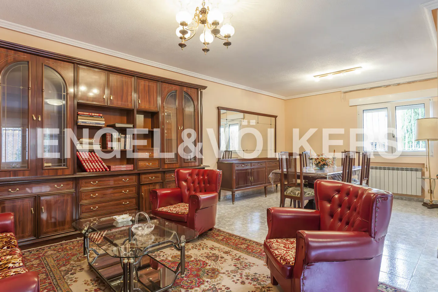 Living room with two red leather armchairs, a glass coffee table, a large wooden wall unit, and a dining area.