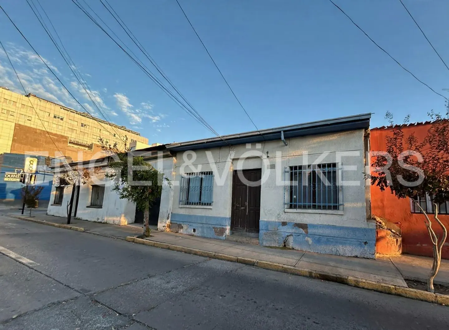 Exterior view of a one-story white house with blue trim and barred windows on a city street.