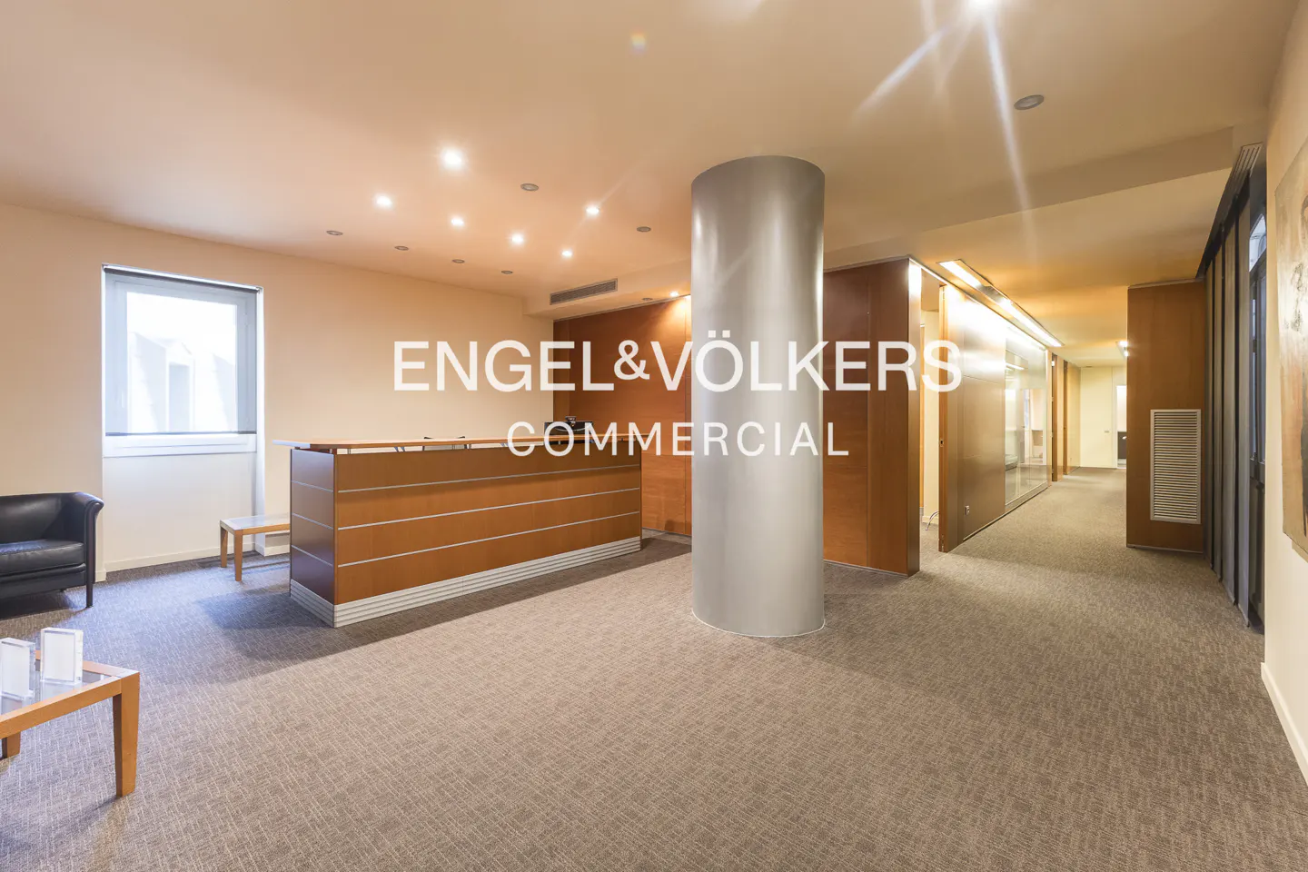 Office lobby with a wood reception desk, gray carpet, and a large gray support column.