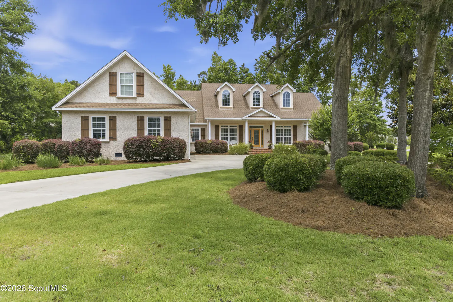 Beige two-story house with brown shutters, a brown roof, and a green lawn on a sunny day.